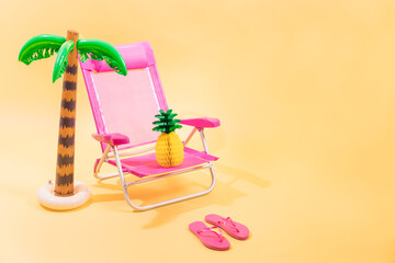 Pink beach chair with a paper pineapple on top of it, pink flip-flops and an inflatable palm tree