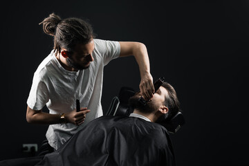 Handsome bearded man has hair and beard cut in barbershop. Dreadlock barber cuts client's hair