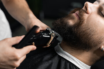 Handsome bearded man has hair and beard cut in barbershop. Dreadlock barber cuts client's hair