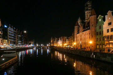 Fototapeta premium A night view on the shores of Martwa Wisla flowing through Gdansk in Poland, with medieval port crane. New architecture meeting with medieval constructions. The city lights reflecting in the river.