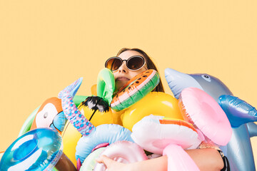 a woman wearing sunglasses surrounded by a lot of inflatables of different shapes and colors on a yellow background.