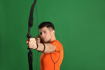 Man with bow and arrow practicing archery on green background, space for text