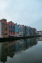 Fototapeta premium A panoramic view on the shores of Martwa Wisla flowing through Gdansk in Poland. The buildings reflect in the calm surface of the river. New architecture meeting with medieval constructions. Overcast