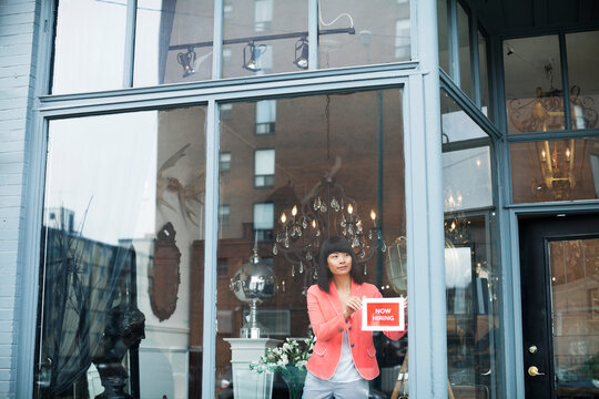 Female Business Owner Displaying Help Wanted Sign In Furniture Store Window