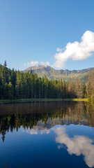 A panoramic view on Smreczynski Staw in Tatra Mountains in Poland. Glacial tarn at the mouth of Pysznianska Valley. The high Tatra chains are reflecting in the calm surface of the lake. White clouds