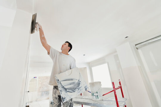 Low Angle View Of Tradesman Plastering Drywall In Home