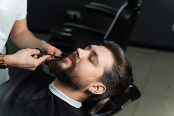 Haircut beard with scissors for a gentleman in a trendy barbershop. Professional hairdresser