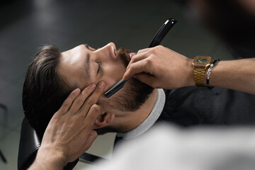 Straight razor cut mans beard in barbershop. Barber man making hairstyle for handsome man.
