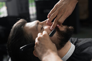 Straight razor cut mans beard in barbershop. Barber man making hairstyle for handsome man.