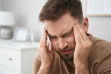 Fototapeta premium Young man suffering from migraine at home, closeup