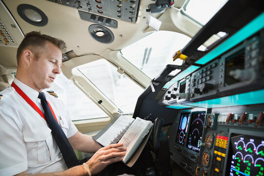 Male pilot checking logbook in airplane cockpit