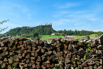 Riegersburg castle in Austria towering above the area. There are wooden logs pilled up in front. Clear blue sky above the castle. The massive fortress was build on the rock. Middle ages