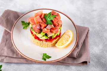 Salmon tartare with tomatoes, avocado and quinoa on a plate and light gray background close up