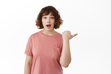 Wow look at this. Amazed caucasian woman pointing right, gasping impressed, checking out announcement, showing cool advertisement, standing over white background