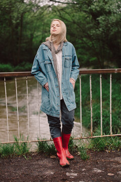 Blonde In Demin Jacket And Red Boots On A Bridge Near River At Country