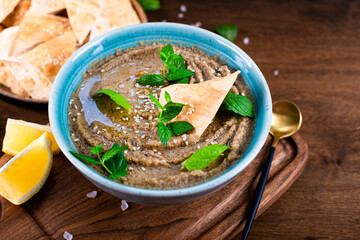  Traditional oriental appetizer baba ganoush with sesame seeds and mint leaves close-up. Eggplant hummus with pita crisps on the wooden table