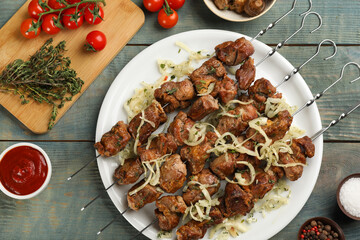 Metal skewers with delicious meat and vegetables served on blue wooden table, flat lay