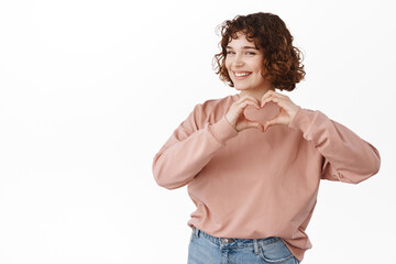 Cute young woman shows heart I love you sign, give compliment, express sympathy or like, standing...