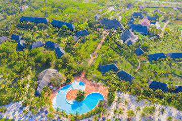 Aerial view of tropical sandy beach with palms and umbrellas at sunny day. Summer holiday on Indian Ocean, Zanzibar, Africa. Landscape with palm trees, hotels, pool, white sand, azure sea. Top view