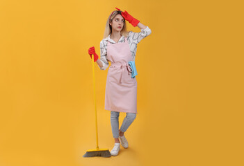 Young housewife with broom on yellow background