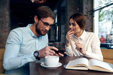 Cheerful man and woman are sitting in a cafe at the table working communication technology