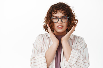 Obraz premium Terrible news. Upset and disappointed young woman with curly hair and glasses, frowning and looking worried, being shocked by something awful, standing against white background