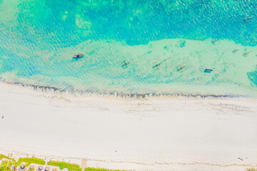 Aerial view of tropical sandy beach with palms and umbrellas at sunny day. Summer holiday on Indian Ocean, Zanzibar, Africa. Landscape with palm trees, hotels, pool, white sand, azure sea. Top view