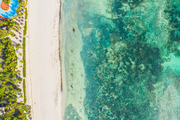 Aerial view of umbrellas, palms on the sandy beach of Indian Ocean at sunset. Summer in Zanzibar, Africa. Tropical landscape with palm trees, parasols, walking people, blue water, waves. Top view