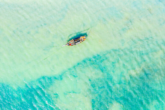 Aerial View Of The Fishing Boats In Clear Blue Water At Sunny Day In Summer. Top View From Drone Of Boat, Sandy Beach. Indian Ocean In Zanzibar, Africa. Landscape With Sailboats, Clear Sea. Seascape