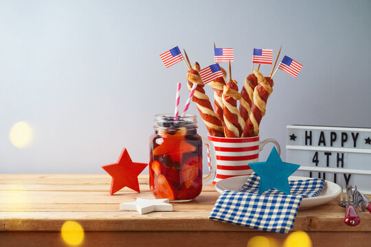 Happy Independence Day, 4th of July celebration concept with summer fresh fruit drink, twisted hot dog sausages and USA flag on wooden table