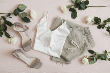 Overhead view of woman's casual spring summer outfit. Jeans, sandals, accessories and flowers on beige background. Flat lay, top view.