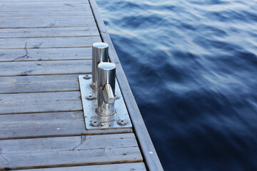 A stainless steel bollard on a wooden pier in the port. Mount for yachts and boats