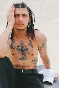 portrait of young man shirtless with tight hair braids and tattoos on skin with copy space white background 