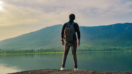 Young man standing near the lake and mountain and enjoying the view of nature - Powered by Adobe