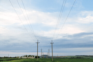 High voltage lines and power pylons in a green agricultural landscape and cloudysky on sunset time background