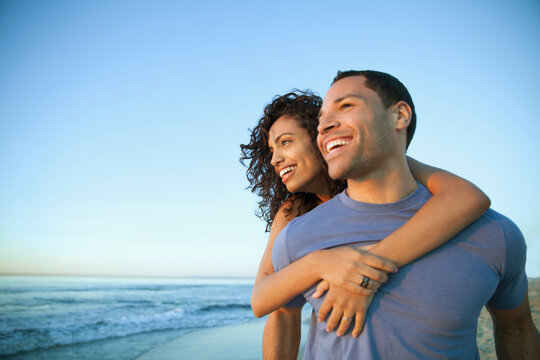 Happy young man giving piggyback ride to woman while looking away at beach