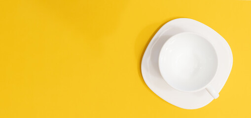 Empty cup on saucer on yellow background with copy space. Drink concept top view directly above of white porcelain ceramic coffee cup