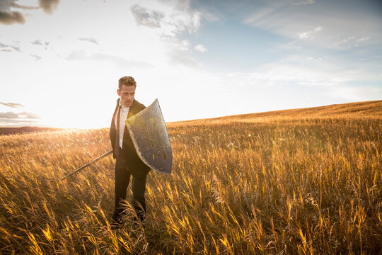 Aggressive businessman with sword and shield in field