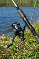 Summer fishing on lake. fishing tackle by river. close-up of fishing rod with spinning reel. The concept of fishing, outdoor recreation.