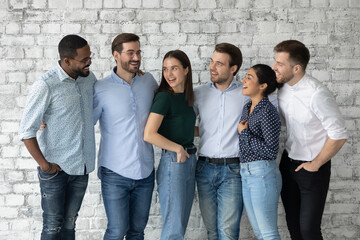 Happy diverse interns or newcomer employees celebrating getting hired, sharing success, hugging, talking, laughing. Smiling people discussing together teamwork. We are like multi racial family