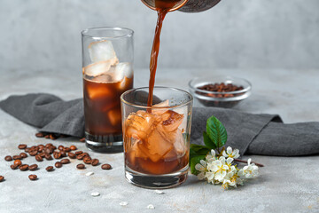 Making iced coffee on a gray background. Pouring coffee into a glass with ice.