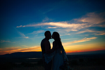 Silhouette of a couple hugging and kissing at sunset against the background of mountains and sea