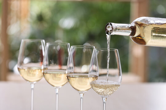 Pouring white wine from bottle into glass on blurred background