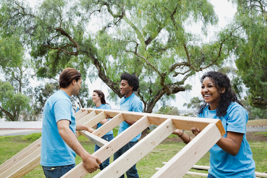 Happy volunteers lifting wooden frame together at park
