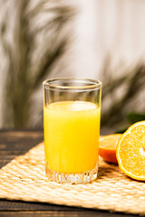 A glass of fresh orange juice on a straw mat and wooden table.