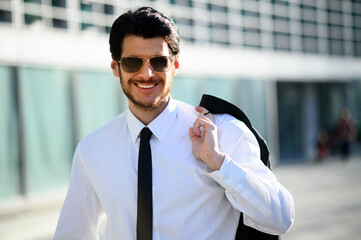 Young businessman outdoor wearing sunglasses and holding his jacket in a sunny day
