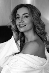 Morning of the bride. Portrait of a girl in negligee. Glamorous photo session on a white bed.
Black and white photo.