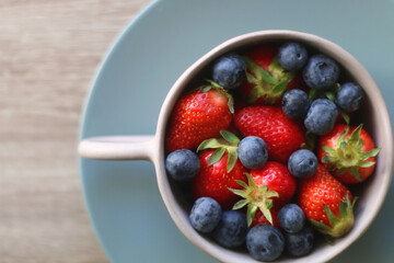 Bowl of blueberries and strawberries on wooden table. Flat lay.