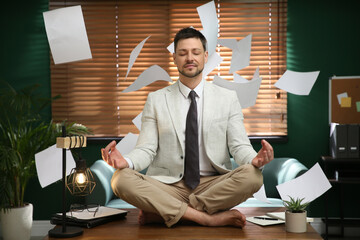 Calm businessman meditating on office desk in middle of busy work day