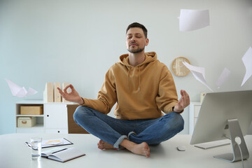 Calm man meditating on office desk in middle of busy work day - obrazy, fototapety, plakaty